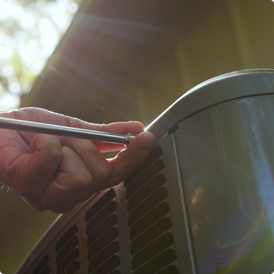 Close-up of a technician running a tool along the fins of an air conditioning condenser