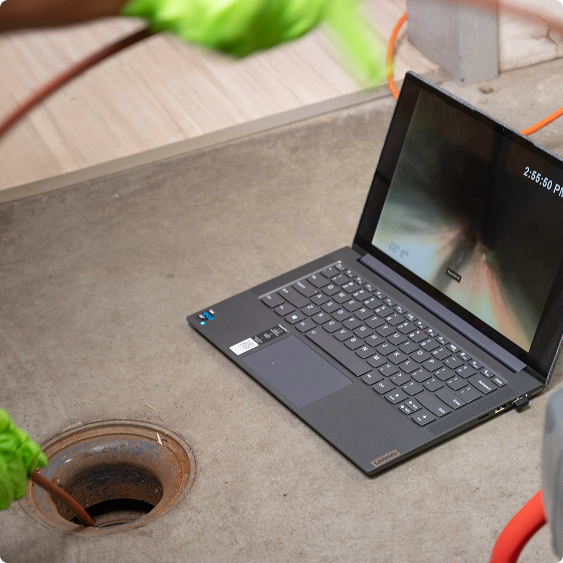 Laptop set up beside an open floor drain during a camera drain inspection