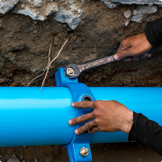 Technician tightening a fitting on a blue water main pipe in an excavated trench