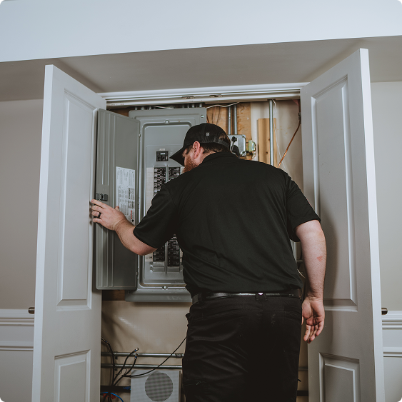 Drake Heating & Air technician troubleshooting an open electrical panel in a home