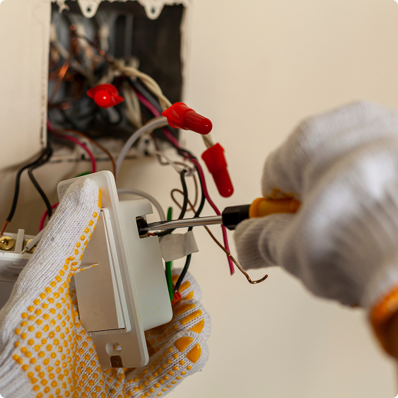 Gloved hands using a screwdriver to work on wiring inside an open electrical box