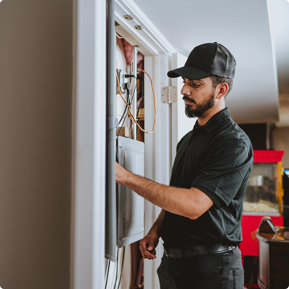Drake Heating & Air technician working at an open electrical panel inside a home
