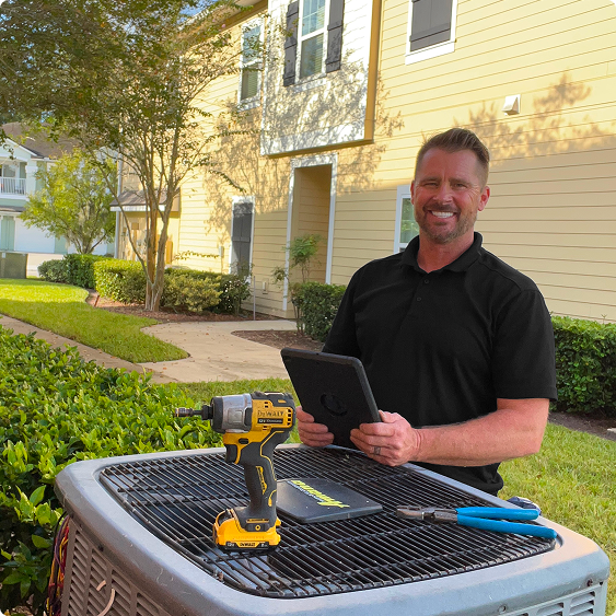 Drake Heating & Air technician with a tablet beside an outdoor air conditioning unit at a Preble County home
