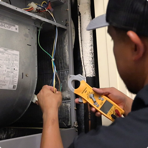 Drake Heating & Air technician testing a furnace with a clamp meter