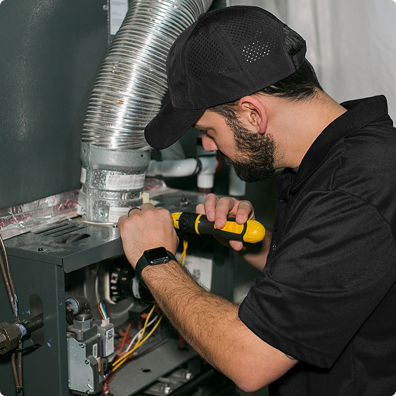 Drake Heating & Air technician securing flue ducting above a furnace with a drill